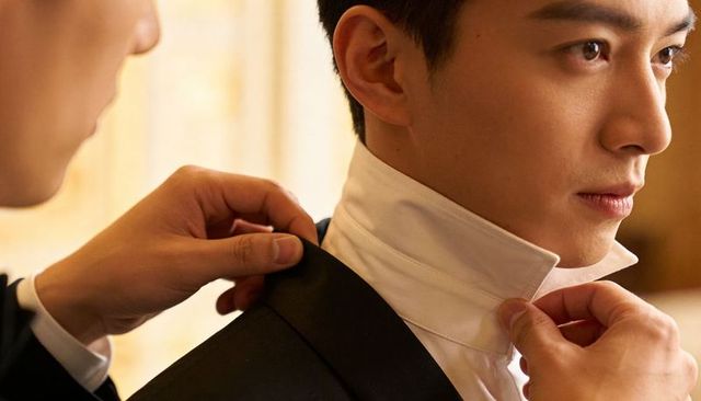 Assistant adjusting high-collar tuxedo on asian groom closeup, wedding preparation detail