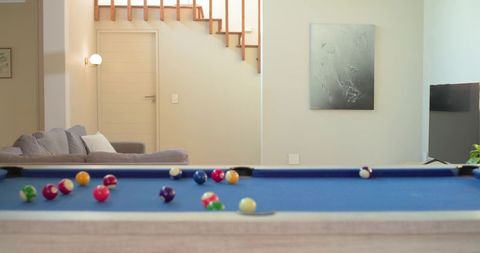 Blue-felt pool table showing scattered billiard balls in modern lounge with neutral decor
