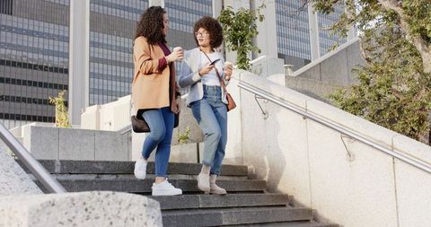 Two Women Walking Down Urban Stairs Holding Coffee and Phone Casual Denim Lifestyle
