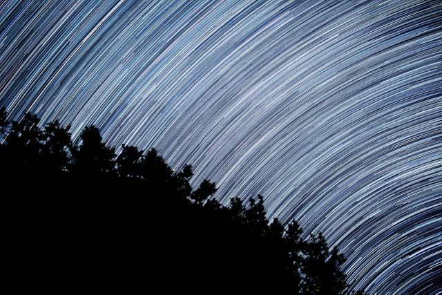 Star trails creating arcs of light across the night sky above a silhouetted forest. Captured with a long exposure, this dramatic scene emphasizes the movement of the Earth and the vastness of the universe. Perfect for use in science presentations, educational materials on astronomy, nature-themed projects, or as a striking wallpaper for those who love astronomy and night photography.