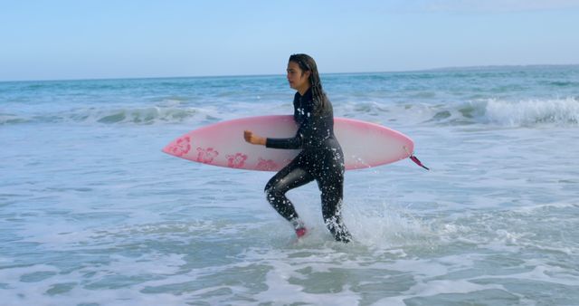 Young biracial woman carries a surfboard at the beach. She's ready for a surfing session in the ocean's waves.