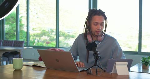 Mid-Adult Man Recording Podcast in Bright Home Workspace with Laptop, Microphone and Tablet