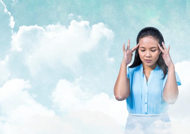 Asian woman in blue blouse, holding head, meditates with closed eyes among clouds. Suitable for themes of mental health, meditation, relaxation, and serenity. Good for wellness websites, meditation apps, and mindfulness promotional materials.