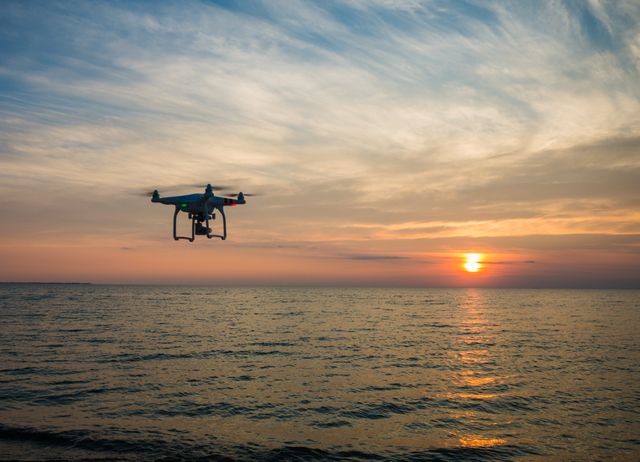 Drone flying over calm ocean during sunset, capturing stunning aerial views. Ideal for use in technology magazines, travel blogs, promotional materials for drone technology, and websites about nature photography or coastal destinations.