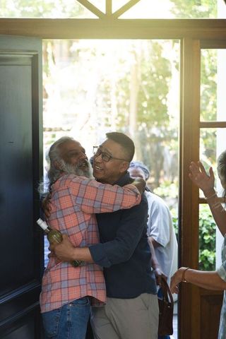 Sunlit reunion: diverse friends embracing at doorway with wine bottle and warm smiles