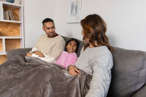 Family cuddling on sofa under plush blanket sharing cozy evening and warm togetherness