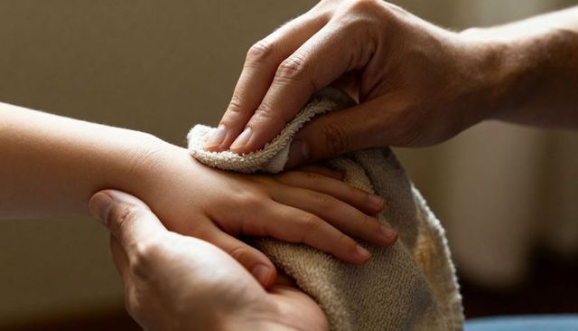 Gentle caregiver hands drying child hand with soft terry towel closeup warmth and care