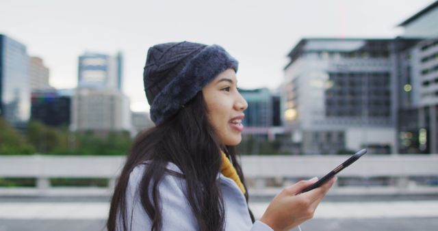 Young woman wearing a hat using a smartphone to explore the city. Ideal for technology, travel, urban lifestyle, and millennial-focused marketing campaigns or blogs.
