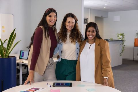 Diverse female team smiling and collaborating at modern business roundtable with tablet