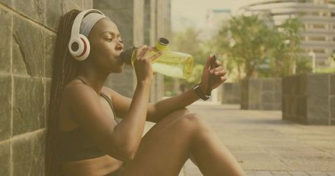 Urban athlete resting: fitness enthusiast with headphones hydrating on city street