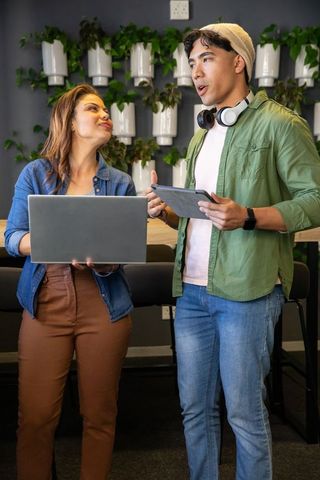 Young diverse coworkers collaborating with laptop and tablet in modern coworking lounge