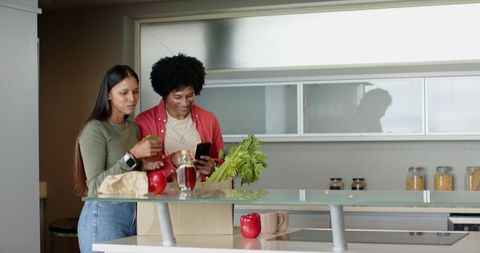 Diverse Couple Unpacking Groceries Sharing Smartphone Moment in Kitchen