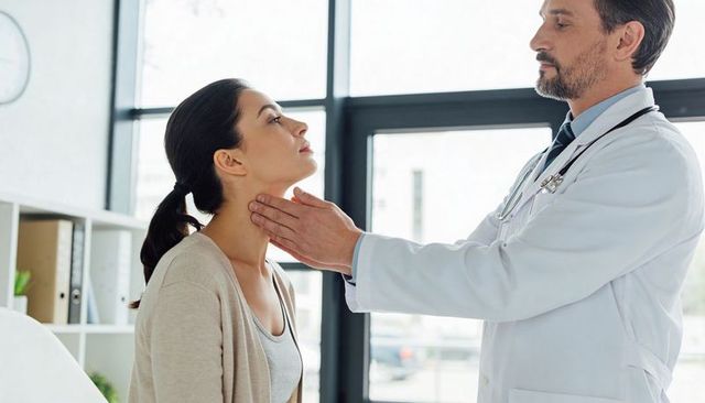 Physician palpating woman's neck during routine exam in bright modern medical clinic