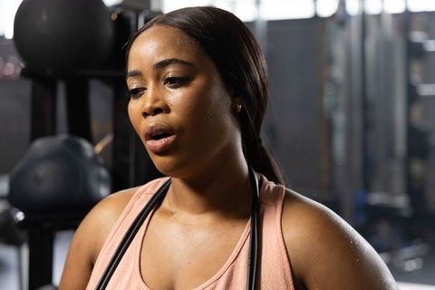 Sweaty african american woman resting after intense jump rope workout in modern gym