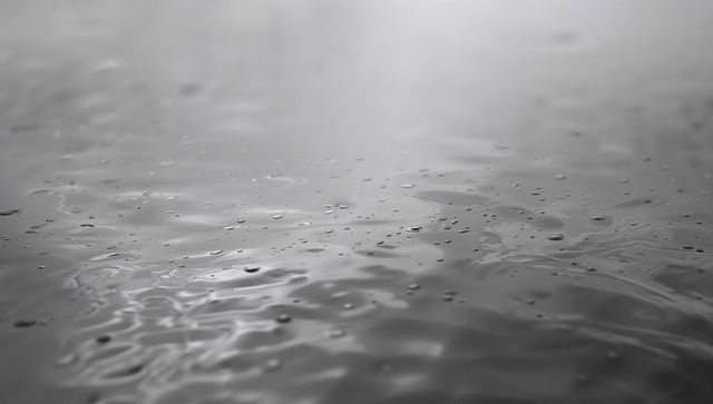 Raindrops creating concentric ripples on monochrome water surface closeup texture