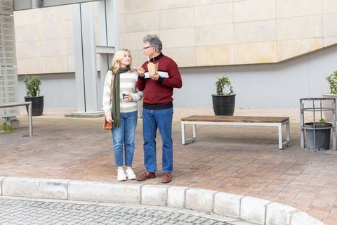 Senior couple strolling and chatting with coffee and takeout in urban plaza