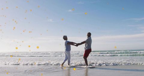 Senior couple holding hands walking in shallow surf with golden light bokeh
