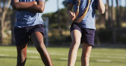 Diverse teen teammates striding on grass field wearing light blue shirts and navy shorts