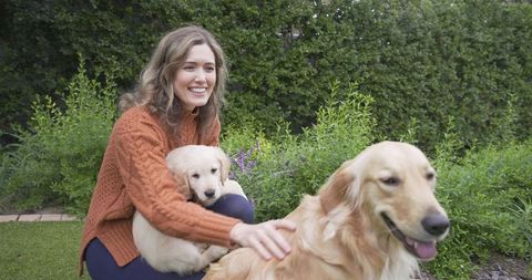Smiling Woman Outdoors with Golden Retriever and Puppy in Garden