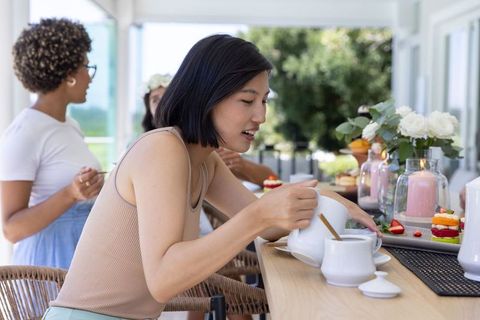 Pouring tea and sharing pastries on sunlit veranda bar with candles and roses