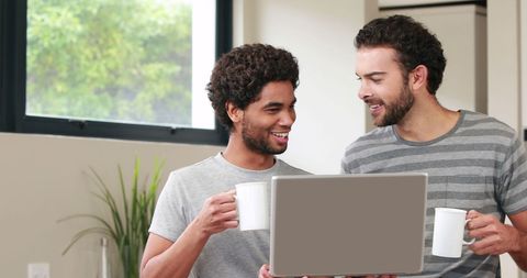 Young diverse men relaxing at home with laptop and coffee