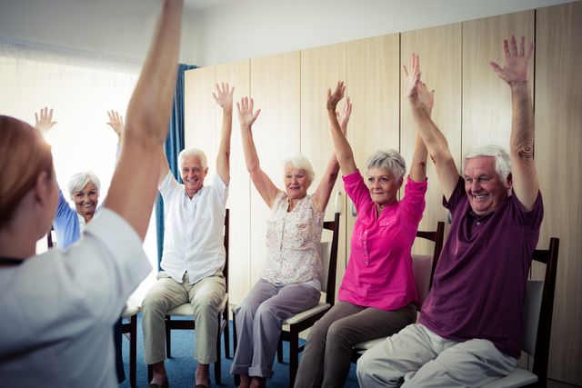 Seniors participating in a group exercise session at a retirement home, raising their arms while seated. This image can be used for promoting senior fitness programs, retirement home activities, healthy aging, and community wellness initiatives.