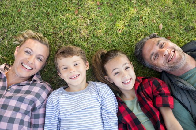 Family enjoying a relaxing day in the park, lying on the grass and smiling. Perfect for use in advertisements, family-oriented content, lifestyle blogs, and promotional materials for parks or outdoor activities.