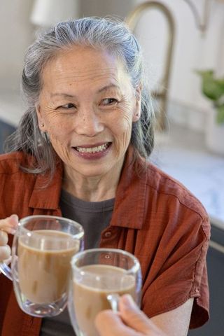 Senior asian woman smiling while sharing coffee at home kitchen counter