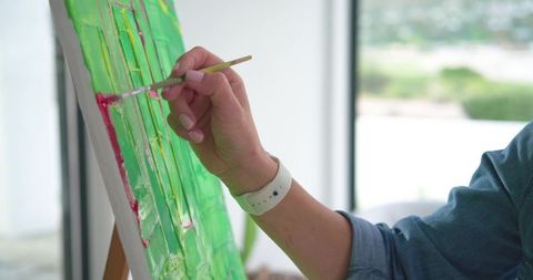 Woman painting vibrant impasto green canvas with red brushstroke in sunlit studio