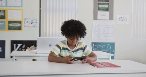 Youth Playing Handheld Console in Classroom Concentrating on Digital Learning and Focused Study