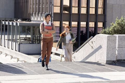 College students walking university campus carrying textbooks and folders in daylight