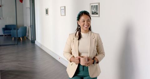 Smiling businesswoman walking in modern office hallway with coffee