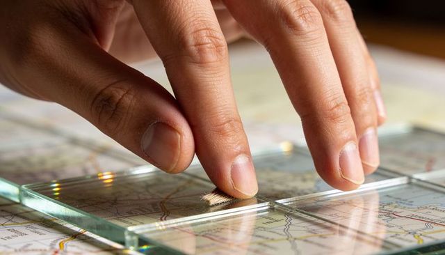 Pressing glass tile over road map with fingertips for map magnifying and route planning