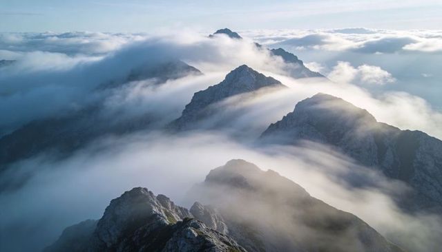 Jagged Alpine Ridge Piercing Low Clouds, Catching Slanted Sunlight over Misty Peaks