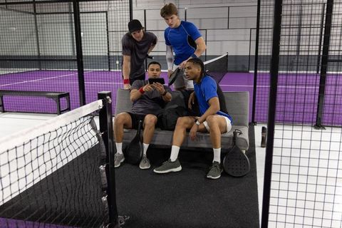 Padel teammates reviewing game footage on smartphone courtside at indoor purple court