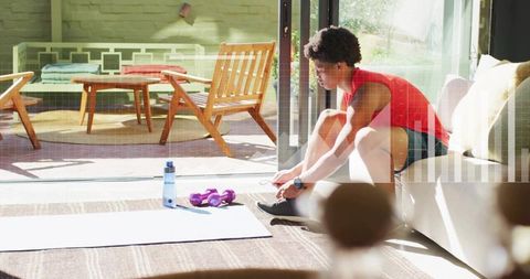 Young man tying sneakers preparing for home workout on sunlit living-room mat