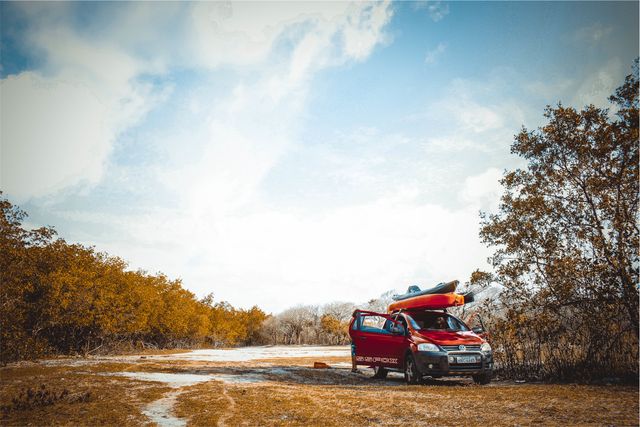 This image of a red SUV parked in an autumn countryside with two kayaks on its roof is perfect for promoting outdoor adventures, camping trips, road trips, and kayak rental services. It also works well for travel blogs, adventure tourism advertisements, and scenic autumn landscape promotions.