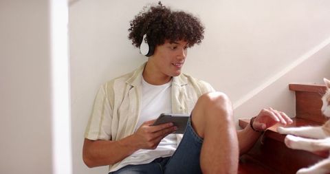 Young Man Relaxing with Headphones and Tablet Petting Cat at Home