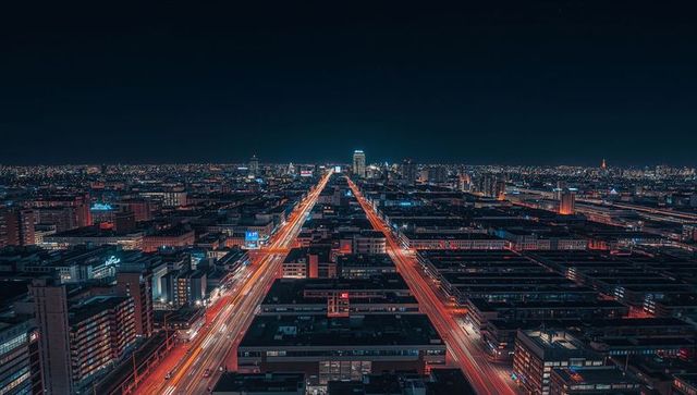 Aerial night cityscape with twin light-trail boulevards converging toward illuminated skyline