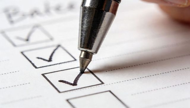Marking checklist with metallic ballpoint pen close-up ticking completed tasks