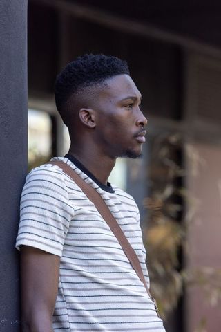 African american man leaning in urban profile wearing striped knit shirt and crossbody