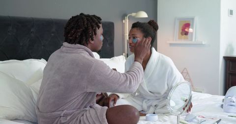 African american couple applying skincare in bed wearing bathrobes intimate pampering