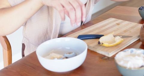 Woman preparing healthy breakfast with banana and yogurt on wooden table morning routine