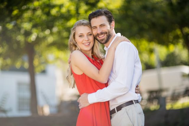 Happy couple hugging and smiling in a restaurant garden with lush greenery in the background. Ideal for use in advertisements, relationship blogs, romantic greeting cards, and lifestyle magazines.