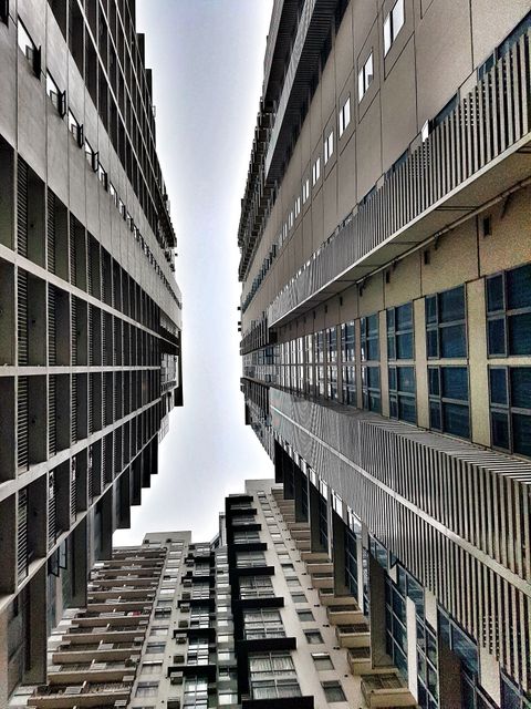 This stock photo captures a dramatic view of two tall, modern buildings with symmetrical architecture from a low angle. Ideal for use in articles, presentations, and websites focusing on urban living, modern cities, architecture, or construction. This image can also be utilized in real estate promotions to showcase modern residential or commercial properties.