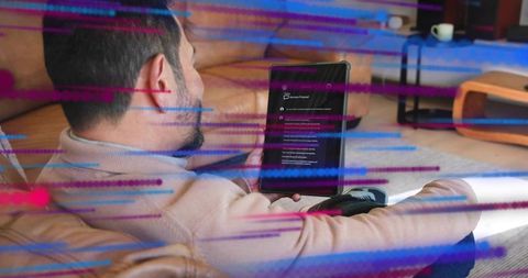 Asian man holding tablet on sofa scrolling digital interface with colorful motion streaks