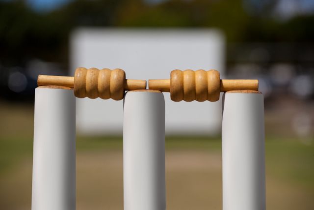 Close-up view of bails resting on top of cricket stumps at a field. Ideal for use in sports-related content, cricket equipment advertisements, or articles about cricket rules and gameplay.
