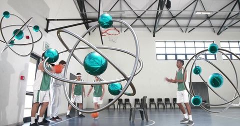 Basketball team warming up with floating metallic orbitals and teal spheres in gymnasium