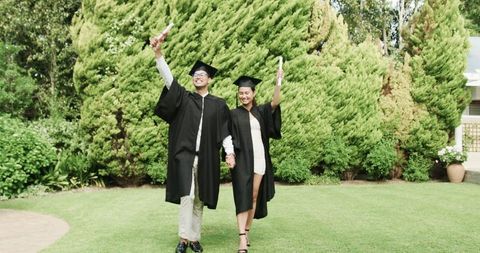 Joyful couples graduation celebration outdoors with diplomas