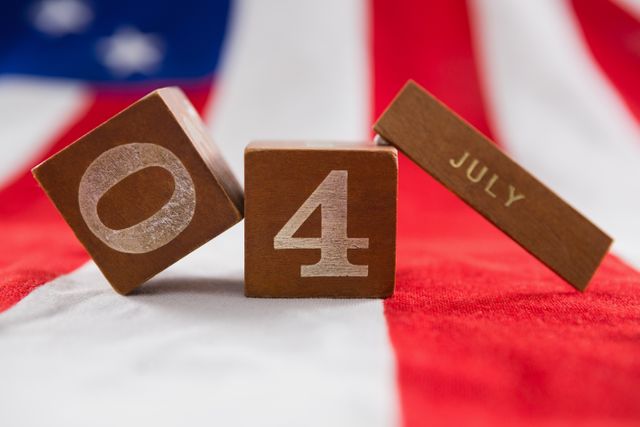 Close-up of wooden date blocks displaying '4' and 'July' on an American flag background. Ideal for use in content related to Independence Day celebrations, patriotic events, and American holidays. Suitable for social media posts, blog articles, and promotional materials for 4th of July events.